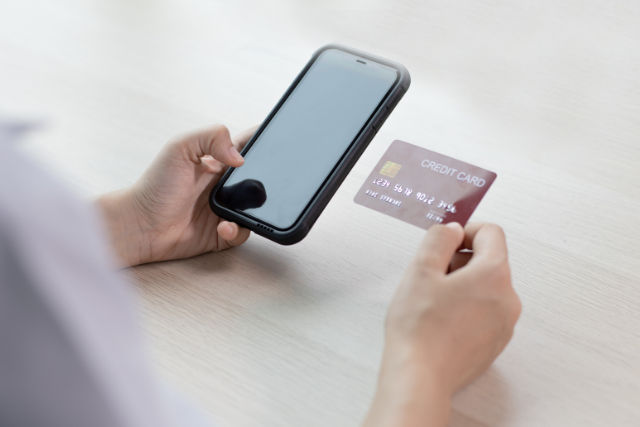 右手にクレジットカード、左手にスマートフォンを持つ女性